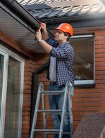 Worker standing on step ladder and repairing gutter on house