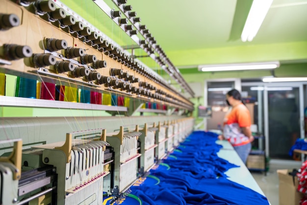 A worker stands in control of a sewing machine Embroidery area in textile factory in industrial zone with modern machinery and technology systems select focus of sewing machine