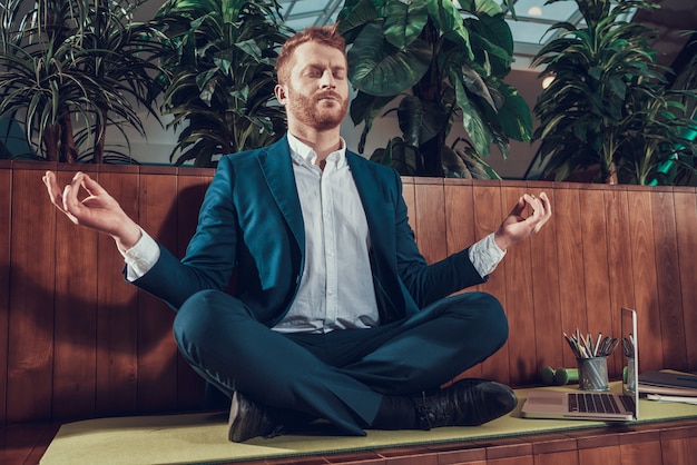 Worker in suit meditating on bench in office.