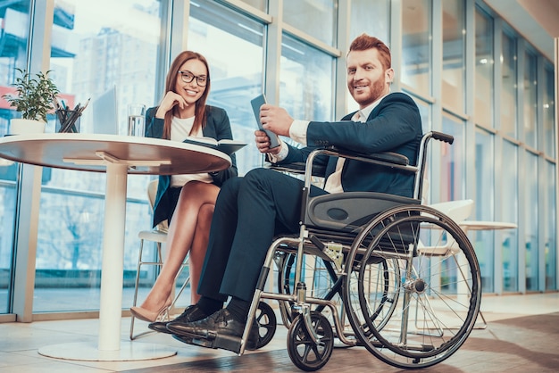 Worker in suit in wheelchair with tablet in office.