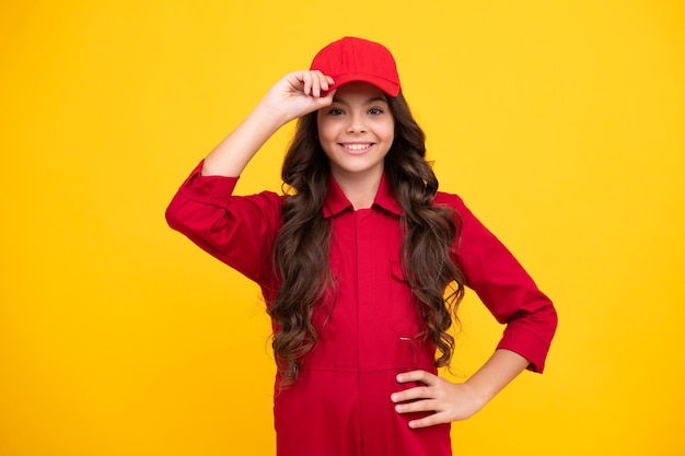 黄色の背景に分離されたオーバー オールと赤い帽子屋内スタジオ ショットを身に着けている労働者 10 代の子供
