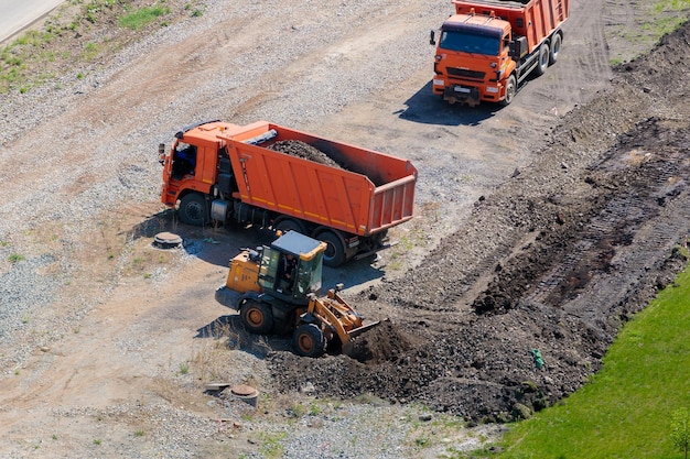 A worker on a tractor with a bucket loads earth into a truck