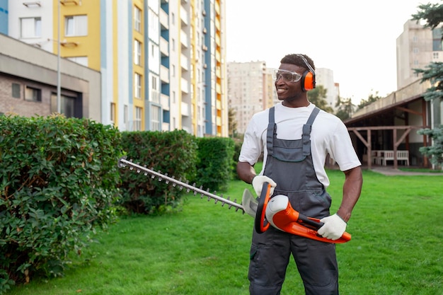 worker in uniform cuts bushes african american man holds electric brush cutter and garden tool