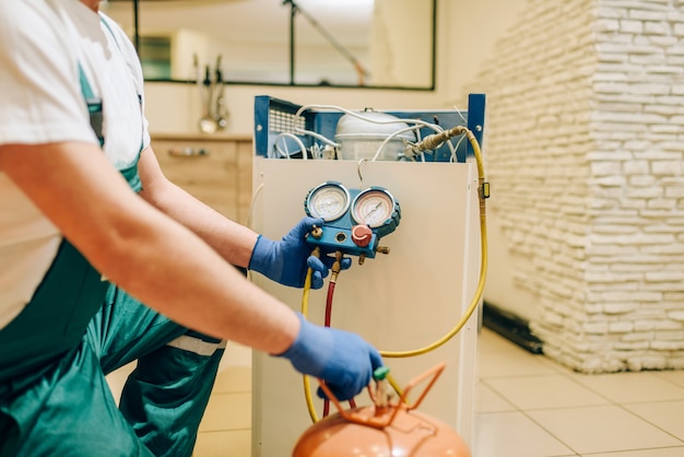 Il lavoratore in uniforme riempie il compressore del frigorifero