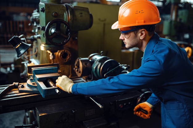 Photo worker in uniform and helmet works on lathe, plant. industrial production, metalwork engineering, power machines manufacturing