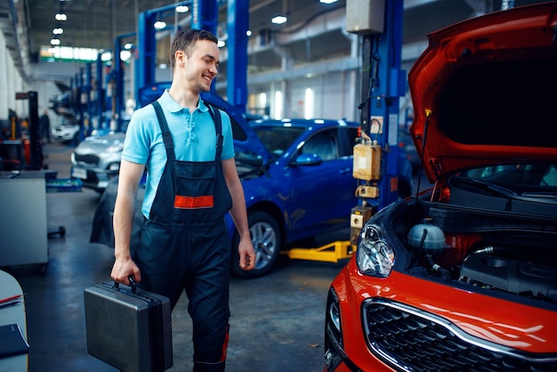 Worker in uniform holds a toolbox, car service station. Automobile checking and inspection, professional diagnostics and repair