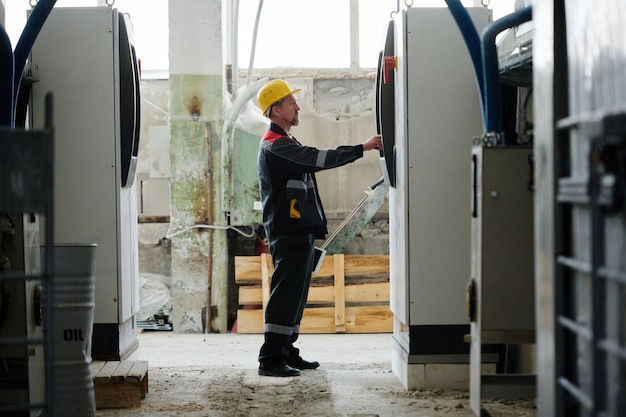 Worker in uniform setting the work of machine standing in workshop