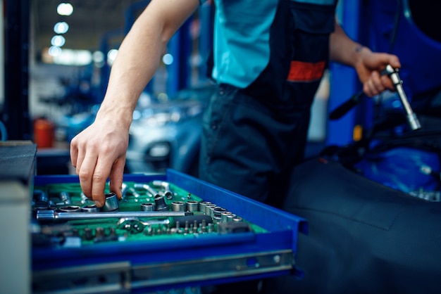 Worker in uniform takes wrench from toolbox, car service station. 