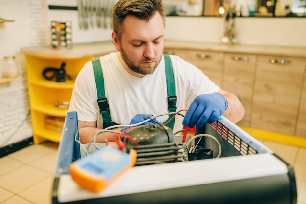 Photo worker in uniform testing refrigerator at home