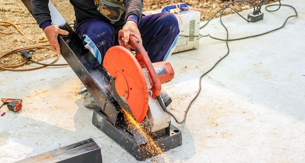 労働者は電気鋼鉄カッターを使用します 建設現場で大きな鋼棒を切断します
