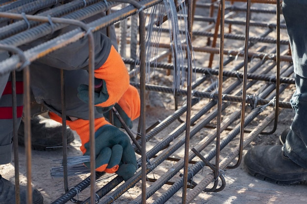A worker uses steel tying wire to fasten steel rods to\
reinforcement bars closeup reinforced concrete structures knitting\
of a metal reinforcing cage