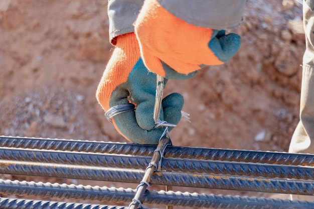 A worker uses steel tying wire to fasten steel rods to\
reinforcement bars closeup reinforced concrete structures knitting\
of a metal reinforcing cage