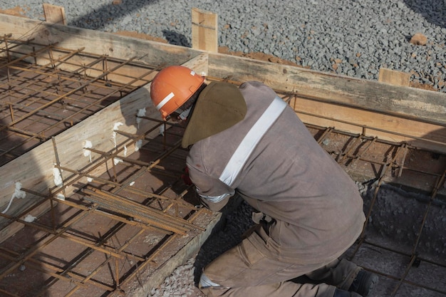 A worker uses steel tying wire to fasten steel rods to\
reinforcement bars reinforced concrete structures knitting of a\
metal reinforcing cage