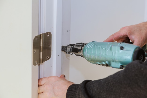 Worker using brad nail gun installs doors Carpenter using a nail gun Air gun for nail gun