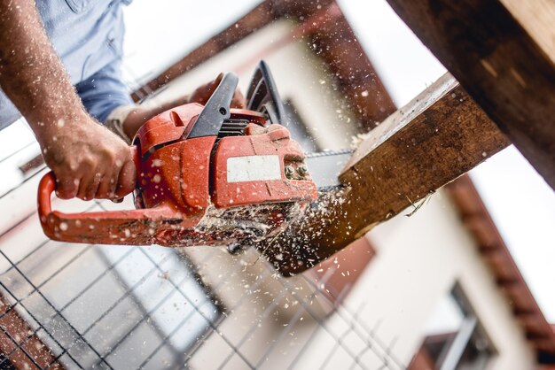 Foto lavoratore che utilizza una motosega per il taglio di legname da costruzione in legno materiale per tagliare e affettare tronchi