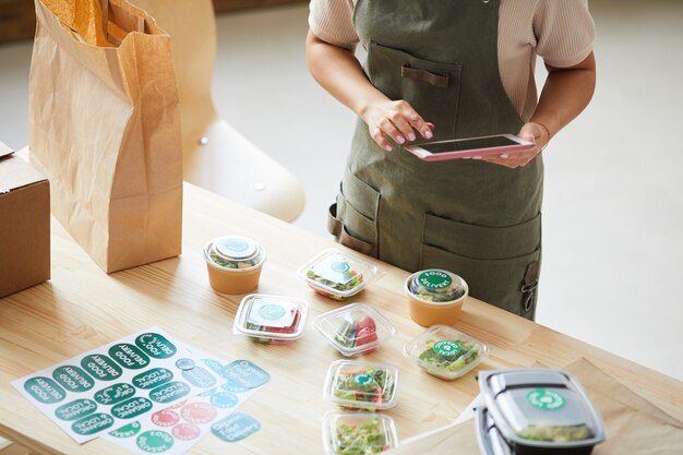 Worker using digital tablet while packaging orders in food delivery service