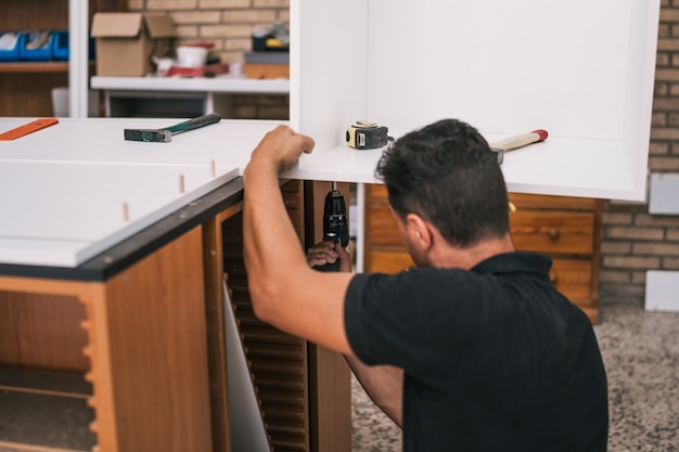 Photo worker using a drill to build a kitchen furniture