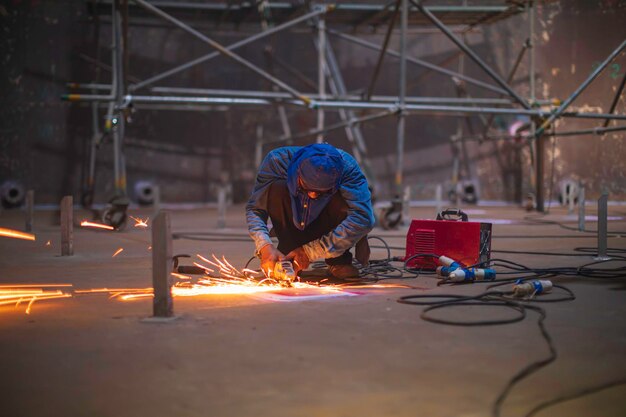 Worker using electric wheel spark grinding metal is part of machinery plate tank beam pipe construction flash spark inside confined