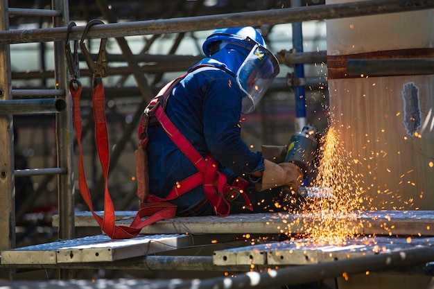 Lavoratore che utilizza la molatura a scintilla della ruota elettrica sul tubo della parte in acciaio al carbonio del metallo della saldatrice all'interno del serbatoio