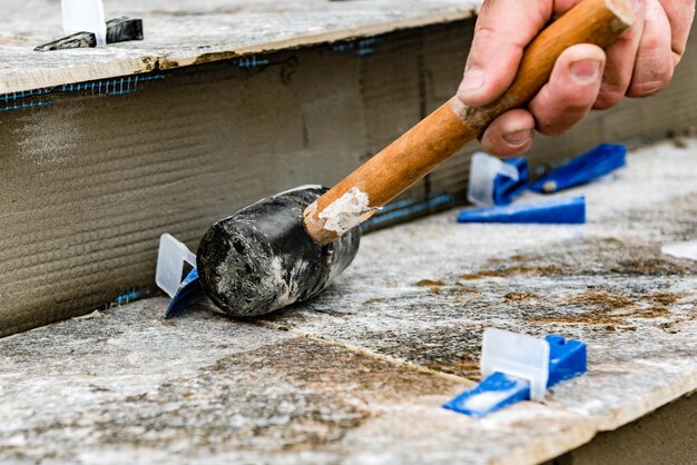 Worker using hammer for removing tile leveling system with plastic clips and wedges.