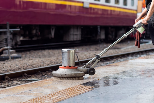 Работник использует скруббер для очистки и полировки пола. Уборка технического обслуживания поезда на железнодорожной станции.