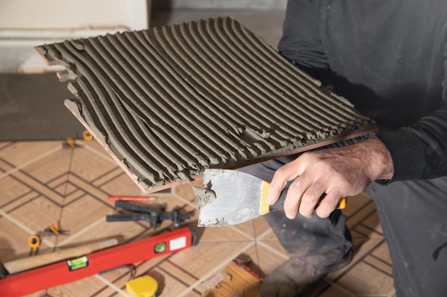 Worker using spatula and putting glue on ceramic tile