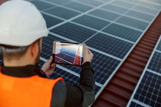 A worker using tablet to take a picture of solar panels on the roof