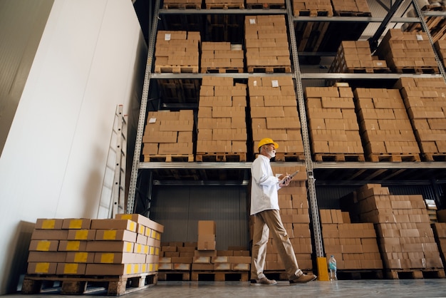 Worker walking in warehouse and using tablet.