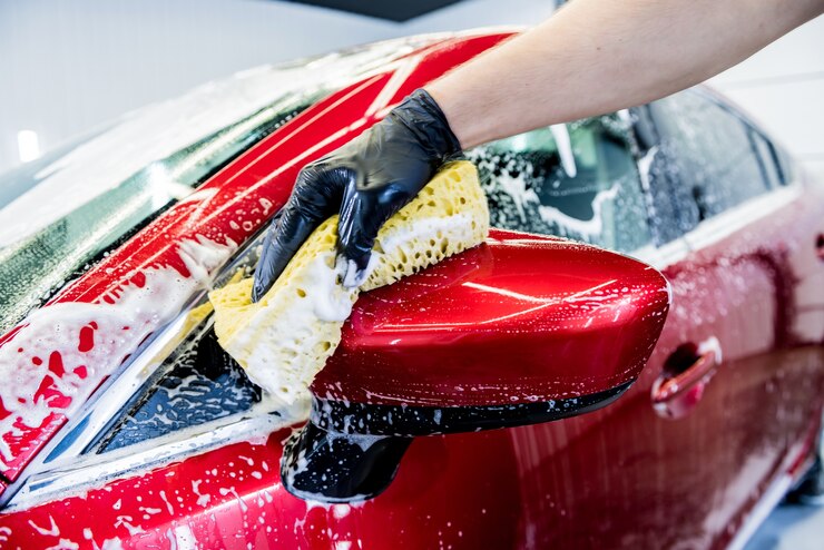 Photo worker washing red car with sponge on a car wash