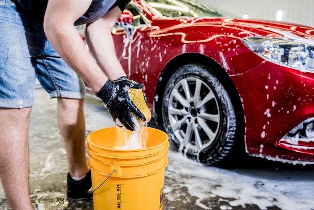 Worker washing red car with sponge on a car wash