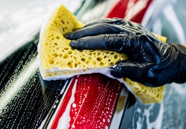 Worker washing red car with sponge on a car wash.