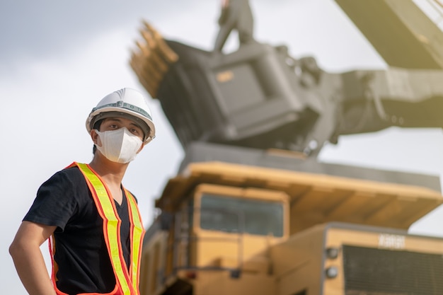 Worker wearing mask in lignite or coal mining with the truck transporting coal.