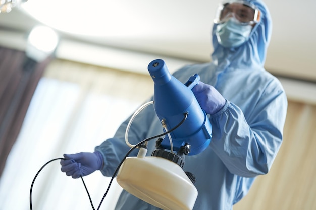 Lavoratore che indossa tute protettive e in piedi con disinfettante