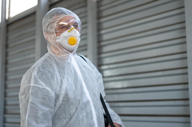 Worker wearing protective suit disinfection gear disinfect surface public place parking. Side view of disinfector safety overall and respiratory mask Covid pandemic disinfection preventive measures