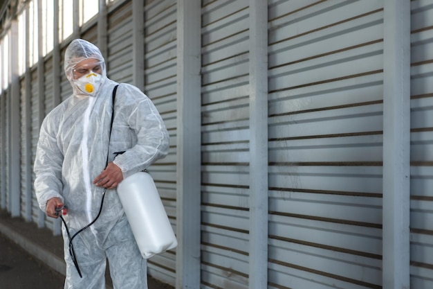 Worker wearing protective suit disinfection gear disinfect\
surface public place parking. side view of disinfector safety\
overall and respiratory mask covid pandemic disinfection preventive\
measures