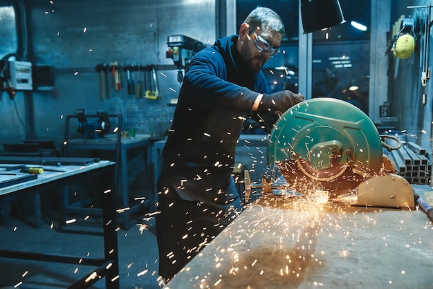 Worker wearing special protective gloves and glasses using grinder to polish piece of metal