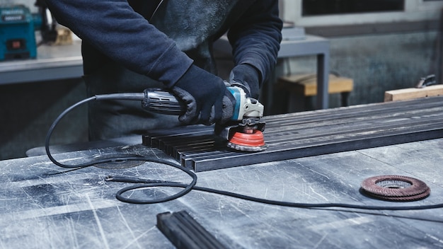 Worker wearing special protective gloves using grinder to polish piece of metal frame