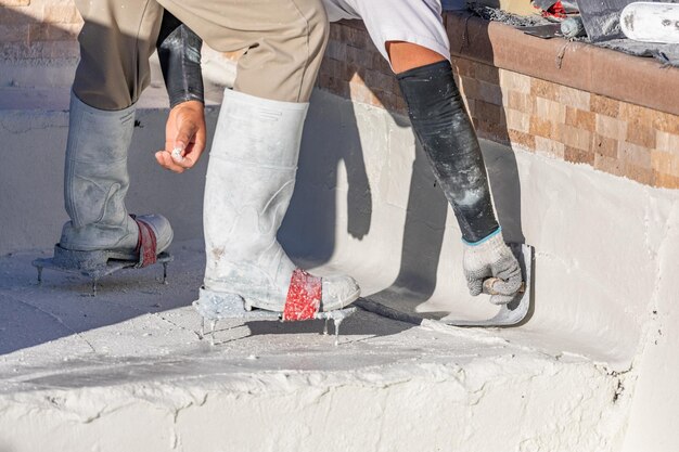 Foto lavoratore che indossa scarpe a spilli che liscia il gesso bagnato della piscina con una paletta