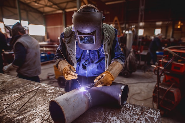 Worker welding iron. Protective suit and mask on. Workshop interior.