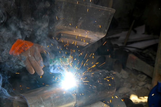 Photo worker welding metal with sparks and smoke in the helmet