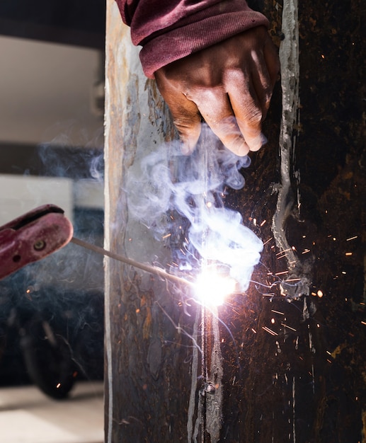 Photo worker welding steel with spark lighting and smoke at construction site