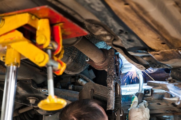 Worker welds the silencer on car by argon welding