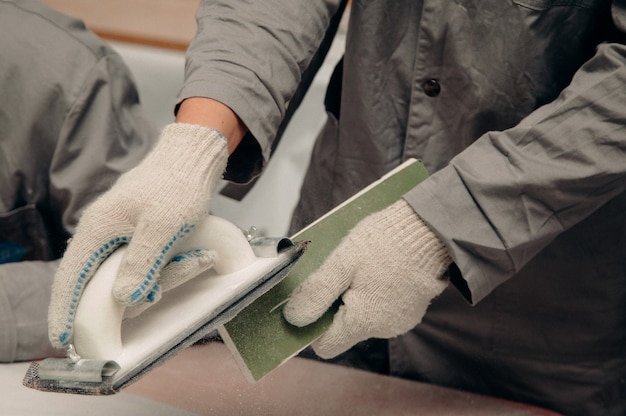 Worker in white gloves strips a wooden blank with sandpaper