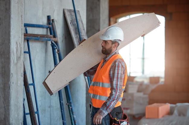 A worker with a beard wearing a protective orange vest and a hard hat while working on a construction site