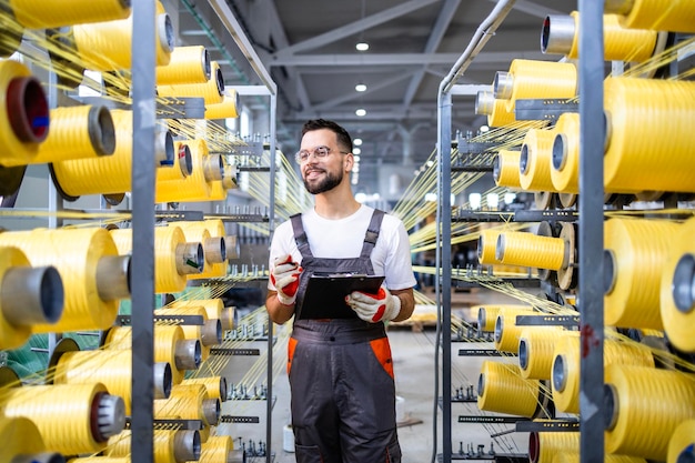 Photo worker with checklist controlling production on knitting machine inside textile factory