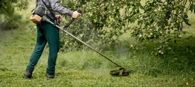 Operaio con una falciatrice a gas nelle sue mani, falciare l'erba davanti alla casa. trimmer nelle mani di un uomo