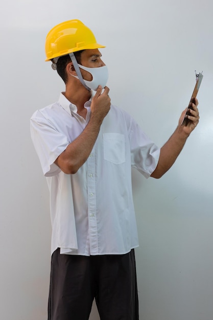 Worker with helmet and pandemic mask isolated on white background. Black man holding spread sheet.