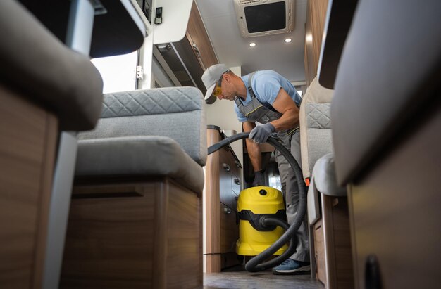 Worker with industrial grade vacuum cleaner cleaning motorhome\
camper van interior