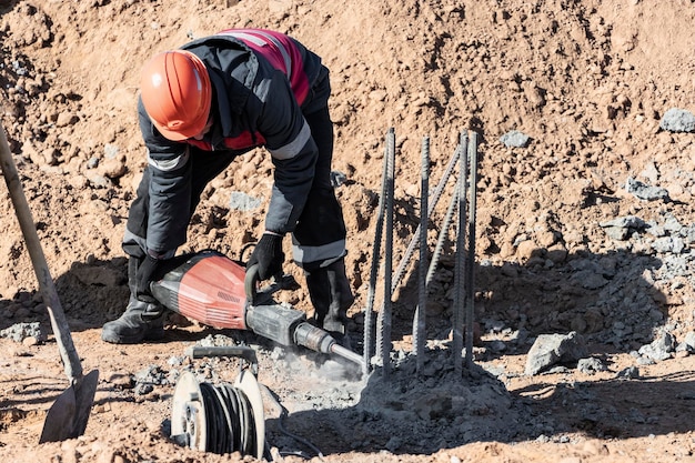 Un lavoratore con un martello pneumatico rompe i pali di cemento abbattimento della testa del palo con un utensile manuale preparazione dei pali per il montaggio della fondazione