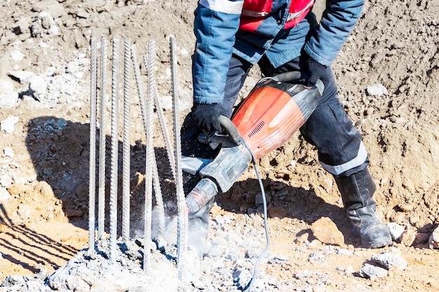 Foto un lavoratore con un martello pneumatico rompe i pali di cemento abbattimento della testa del palo con un utensile manuale preparazione dei pali per il montaggio della fondazione